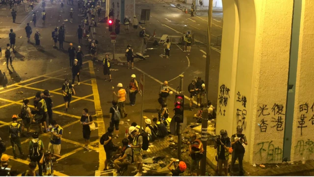 示威者纷纷撤退，留下墙上的涂鸦，满地狼藉，远处的警察仍然站在那里待命。