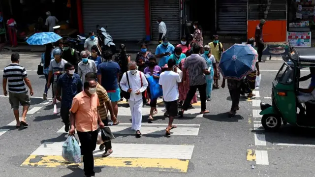 Residents wearing facemasks cross a road in the central Sri Lankan town of Pilimathalawa on May 5, 2020, during a break in the curfew that was first imposed on March 20. - Sri Lanka says it will start easing lock down restrictions from May 11 and claims that the spread of the coronavirus was well under control with eight deaths and 755 infections in the nation of 21 million.