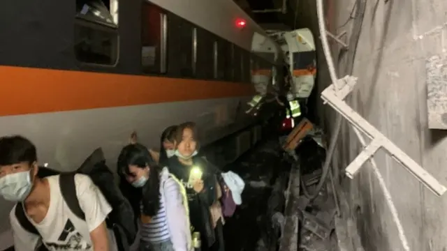 People walk next to a train which derailed in a tunnel north of Hualien