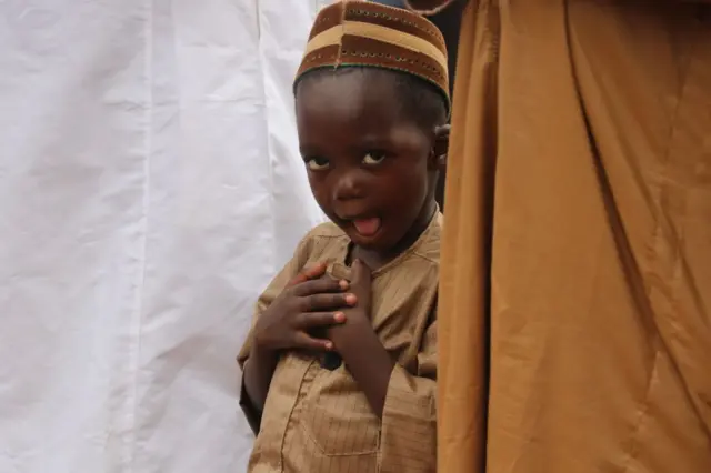 A young boy makes a funny face at the camera during prayers.