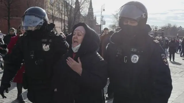 একজন নারীকে বিক্ষোভ থেকে সরিয়ে দিচ্ছে দাঙ্গা পুলিশ।