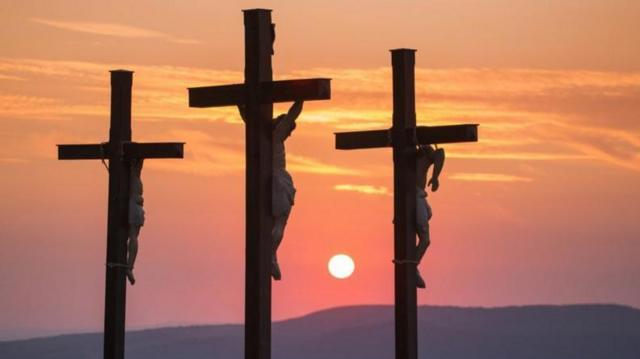 Três pessoas crucificadas com o pôr do sol ao fundo