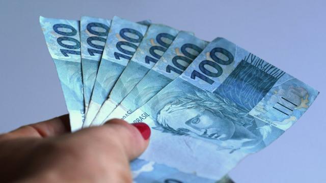 Mão de mulher segurando notas de 100 reais
