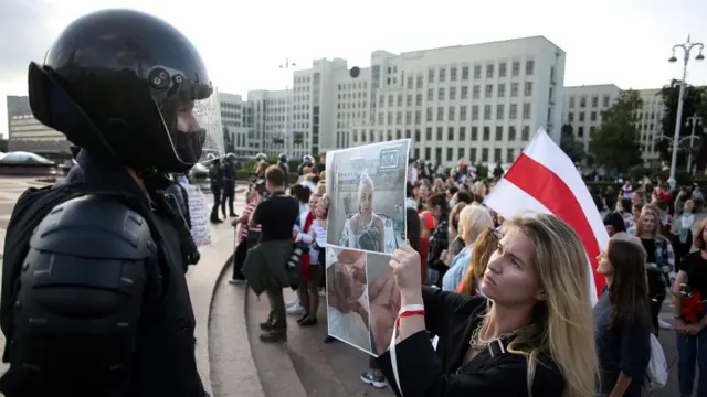 Участница демонстрации в Минске показывает фото пострадавших во время протестов