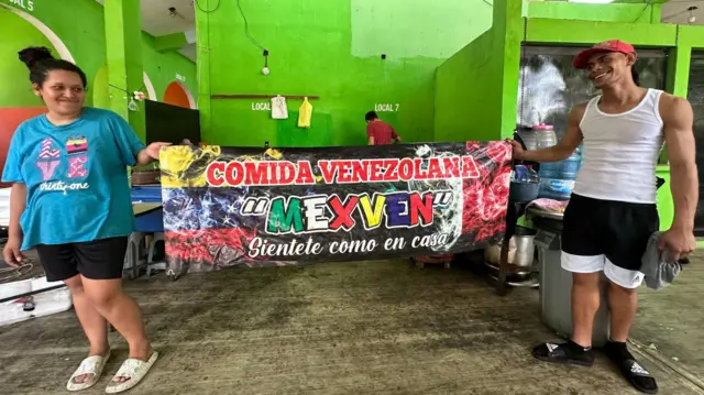 Los trabajadores de MexVen mostrando el cartel de promoción del local. 