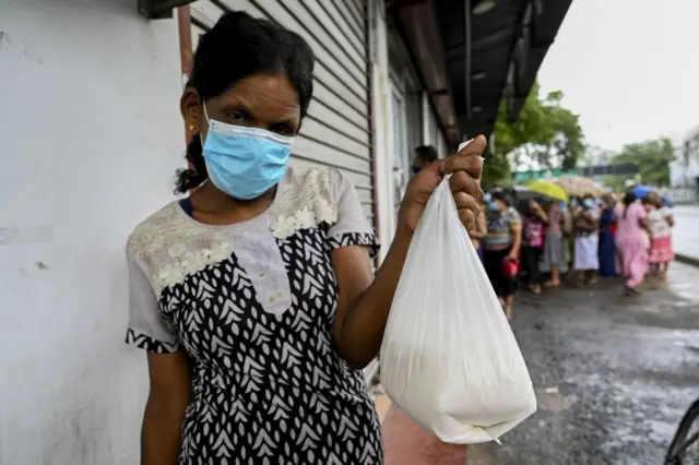 Woman shows her food packet while others behind her wait in queue