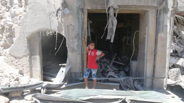 Halep'te bir saldırı sonrası yıkıntıların önünde ayakta dikilen çocuk