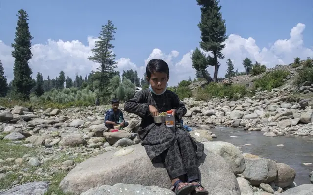 झरने के पास बैठकर लंच करता एक बच्चा