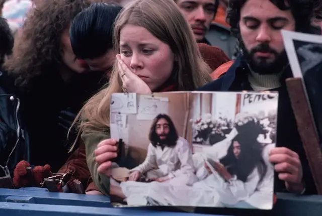Jóvenes apesumbrados con una foto de John Lennon, lamentando su muerte
