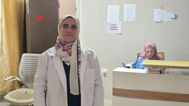 القابلة سحر عادل عقل ترتدي معطفها الأبيض، وتقف داخل أحد المراكز الطبية 