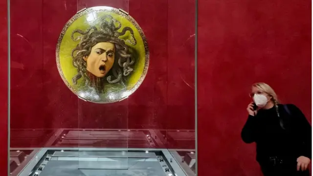 زائرة تنظر حول الجزء الخلفي من اللوحة الأيقونية "تيستا دي ميدوزا" لكارافاجيو والتي يرجع تاريخها إلى حوالي عام 1597