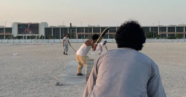 Migrantes jogando críquete0 betfrente a um campo aberto