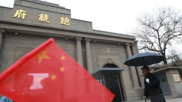 A impersonator of Chiang Kai-shek, right, talks with tourists, with a national flag of the People's Rebpulic of China at front held by a tourist, at the old Presidential Palace in Nanjing, Jiangsu province