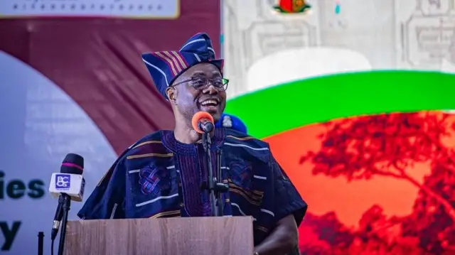 Gomina Seyi Makinde wọ aṣọ ofi, gbohungbohun wa niwaju rẹ, o n wo ẹgbẹ to si n rẹrin-in