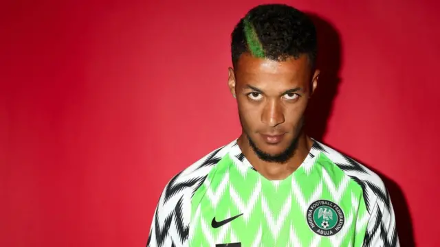 William Troost-Ekong con el pelo ondulado corto y una franja pintada de verde en el lado derecho