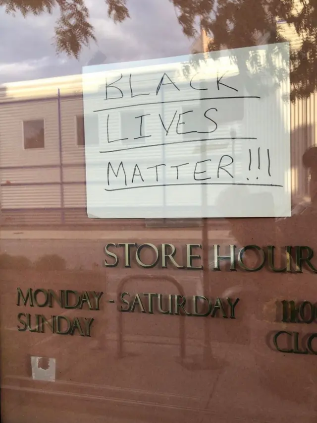 แผ่นป้ายที่เขียนข้อความ "BlackLivesMatter" ที่มีความหมายว่า "ชีวิตคนดำมีค่า" ปิดหน้าร้านผ้าม่าน ซึ่งเป็นร้านของเพื่อนจิรัญญา