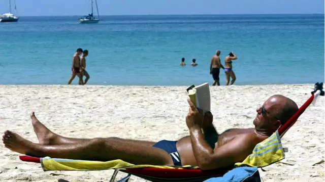 Bir turist Phuket adasındaki Kata plajında kitap okuyor.