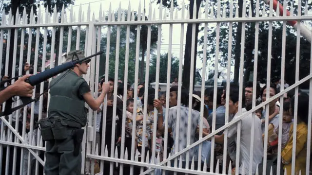 Infantes de la Marina de EE.UU. resguardan la entrada de la embajada en Saigón, mientras una multitud de vietnamitas espera ser evacuada