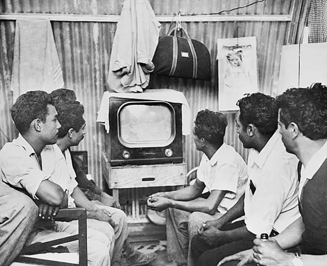 En sus humildes barracas después de un duro día de trabajo, los braceros se relajan mirando la televisión. Los hombres juntaban sus ganancias para comprar el set.