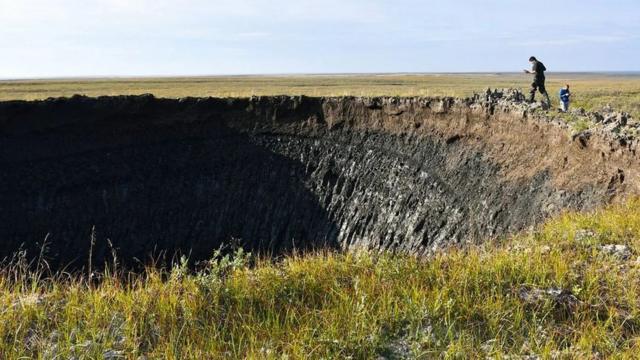 Imagem do cientista Evgeny Chuvilin analisando a borda de uma das crateras, um grande buraco negro na tundra