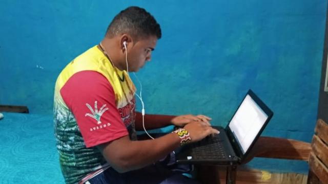Leonel mexejogar pela internet caixanotebook enquanto acompanha aula online. Ele está sentado na cama e com um fonejogar pela internet caixaouvido.