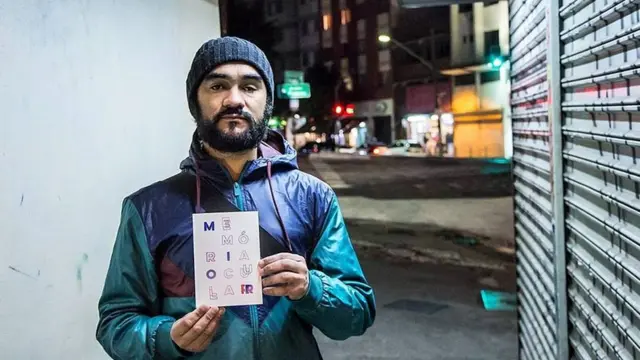 Sérgio Silva no cruzamento em que foi alvejado, segurando livro escrito sobre o ocorrido, Memória Ocular, do jornalista Tadeu Breda