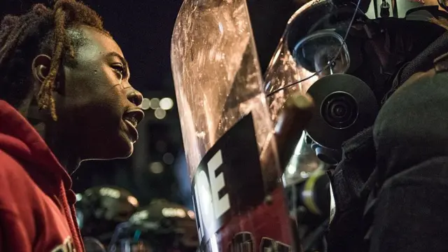 Mujer negra enfrentándose a un policía durante una protesta.