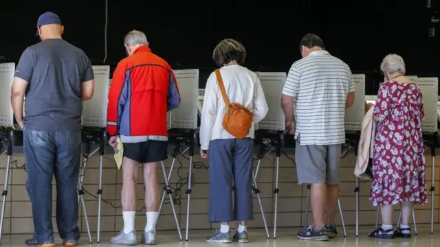 Votantes de espaldas emitiendo su voto.