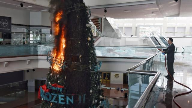 A person tries to extinguish a burning Christmas tree after protesters set fire to it at Festival Walk shopping mall in Kowloon Tong, Hong Kong, China, 13 November 2019. Hong Kong is in its sixth month of mass protests that were originally triggered by a now withdrawn extradition bill, which have since turned into a wider pro-democracy movement.
