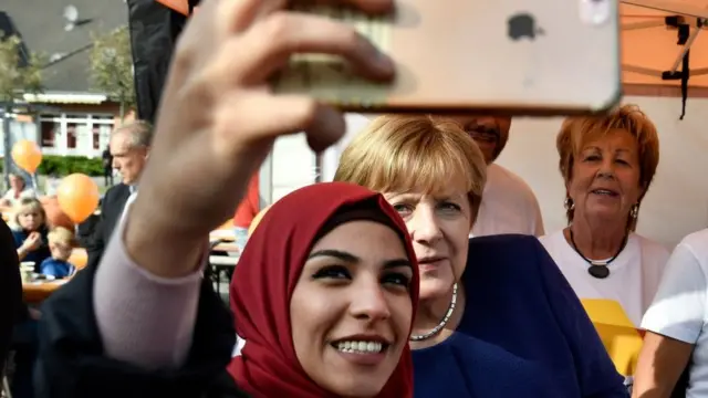 Inmigrante tomándose una foto con Angela Merkel.