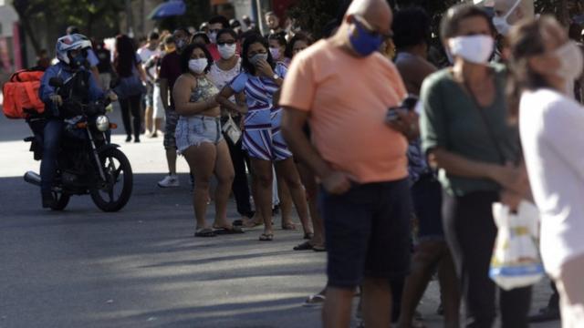 Dezenas de pessoas com máscaras enfileiradas em rua do Rio de Janeiro