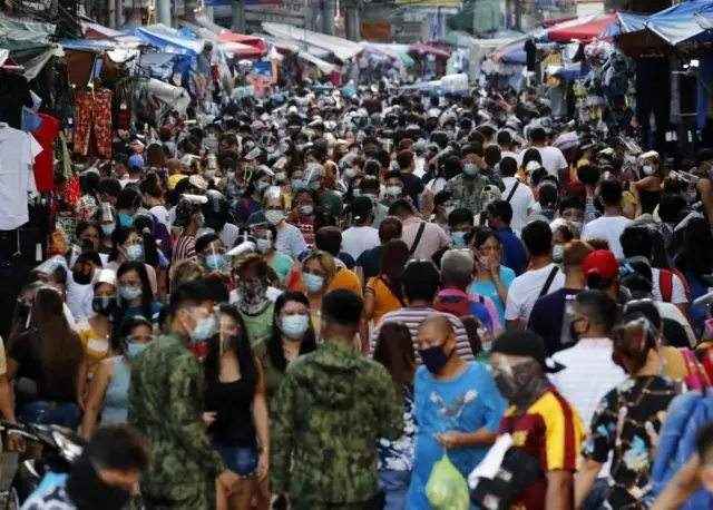 A crowd of shoppers next to makeshift stores to choose from an assortment of items sold at bargain price along a road in Manila, Philippines, 23 December 2020