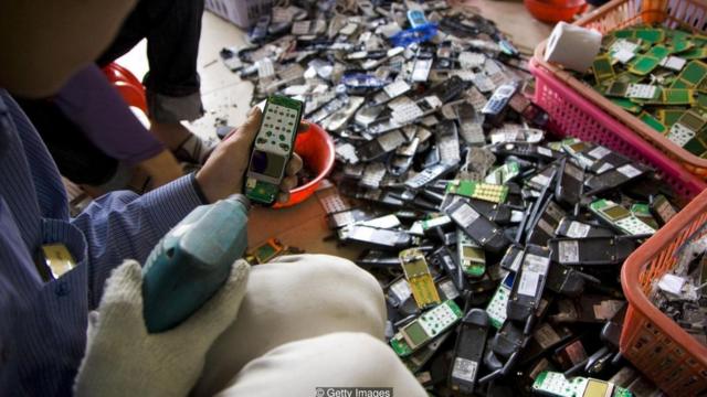 Trabalhador desmonta celular depósito de lixo da cidade de Guiyu, na China