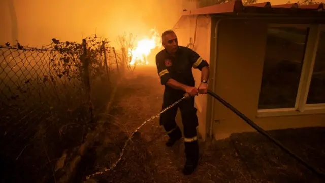 Un bombero intenta acerca una manguera para sofocar un incendio en una casa de la isla griega Evia.