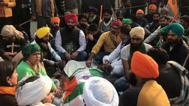 போராட்டத்தின்போது உயிரிழந்ததாக கூறப்படும் விவசாயியின் உடலில் தேசியக் கொடியை போர்த்தி வைத்து சூழ்ந்து அமர்ந்துள்ள சக விவசாயிகள்