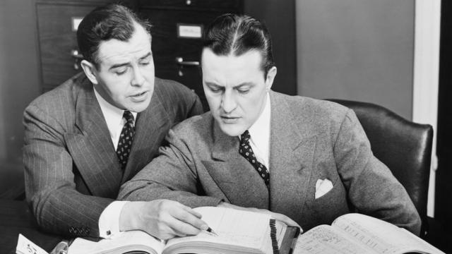 Image en noir et blanc de deux hommes vérifiant des livres de comptabilité