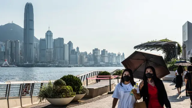 香港尖沙咀海旁两位戴着口罩的女士撑着雨伞遮挡阳光（24/7/2022）