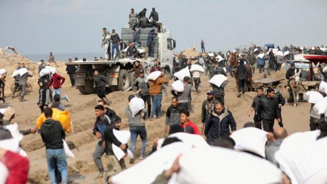 巴勒斯坦人抗着从以色列检查站附近的一辆援助卡车上抢来的面粉袋。