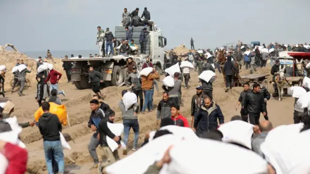 巴勒斯坦人抗著從以色列檢查站附近的一輛援助卡車上搶來的麵粉袋。