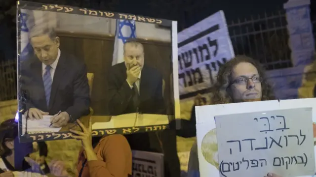 یک معترض در تل آویو پوستری در دست دارد که در آن تصویر نتانیاهو در کنار آویخای مندلبلیت، دادستان کل اسرائیل. مخالفان بی‌بی خواستار محاکمه او به اتهام فساد مالی هستند