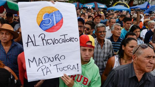 Un joven alza una pancarta que dice "Sí al revocatorio. Maduro pa' fuera"