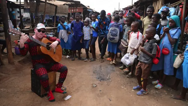 Lazare joue de la guitare devant une petite foule dans la rue.
