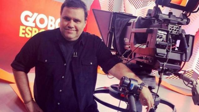 O apresentador Rodrigo Rodrigues posa em estúdio de TV ao lado de câmera
