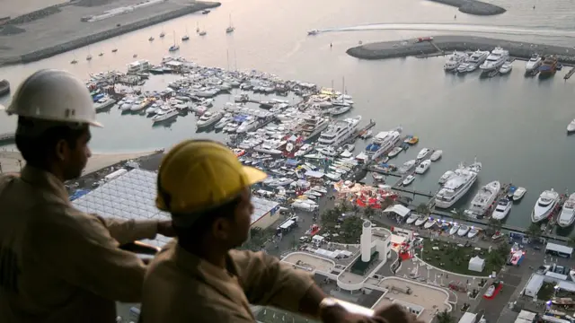 Indian workers watch the openning of Dubai's international boat show from the 50th floor of the tower which is beign constructed behind the Dubai International Marine Club, 14 March 2006.