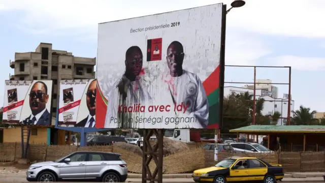 Des voitures passent sous les pancartes de campagne des candidats à la présidentielle au Sénégal.
