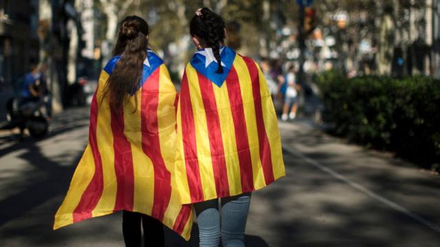 Dos jóvenes caminan por Barcelona envueltas en banderas independentistas de Cataluña.