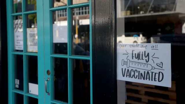 Магазин на улице Окленда. Объявление на двери магазина: "Весь наш персонал полностью вакцинирован"