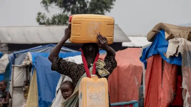 Une femme porte deux jerricans d'eau pour approvisionner son abri dans le camp pour personnes déplacées de Kayembe, près de Goma, le 30 août 2021.
