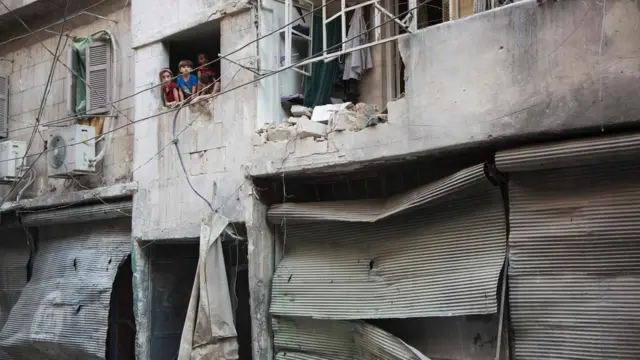 Doğu Halep'te kısmi olarak yıkılmış bir binanın camından bakan çocuklar.