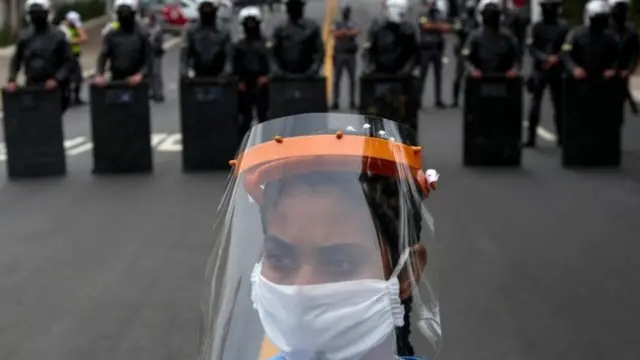 Woman in mask and face shield in front of police